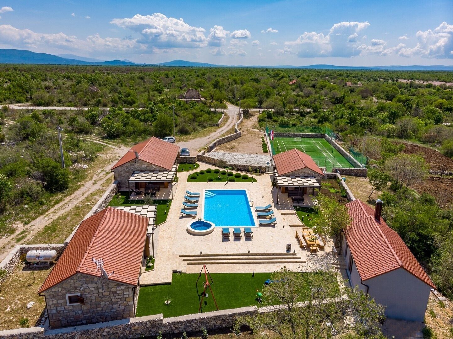 A villa with a swimming pool, tennis court, and stone buildings.