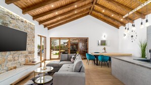 Uma sala de estar moderna com parede de pedra, sofá modular cinza, mesa de centro redonda e teto de madeira.