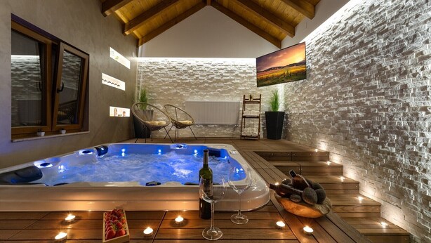 Uma área de spa com hidromassagem, piso de madeira, paredes de pedra e uma televisão fixada na parede.