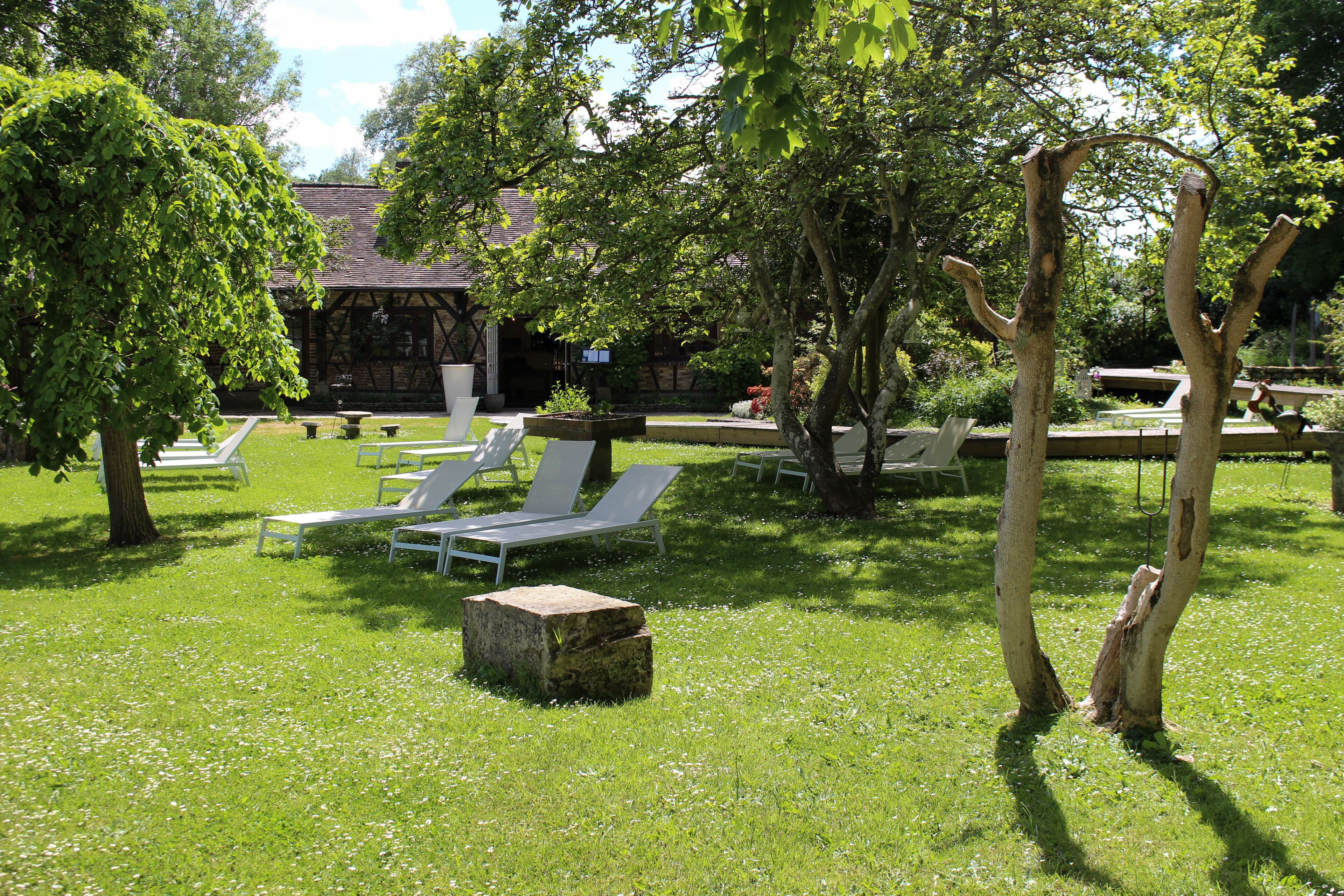 A garden with white lounge chairs and a stone bench.
