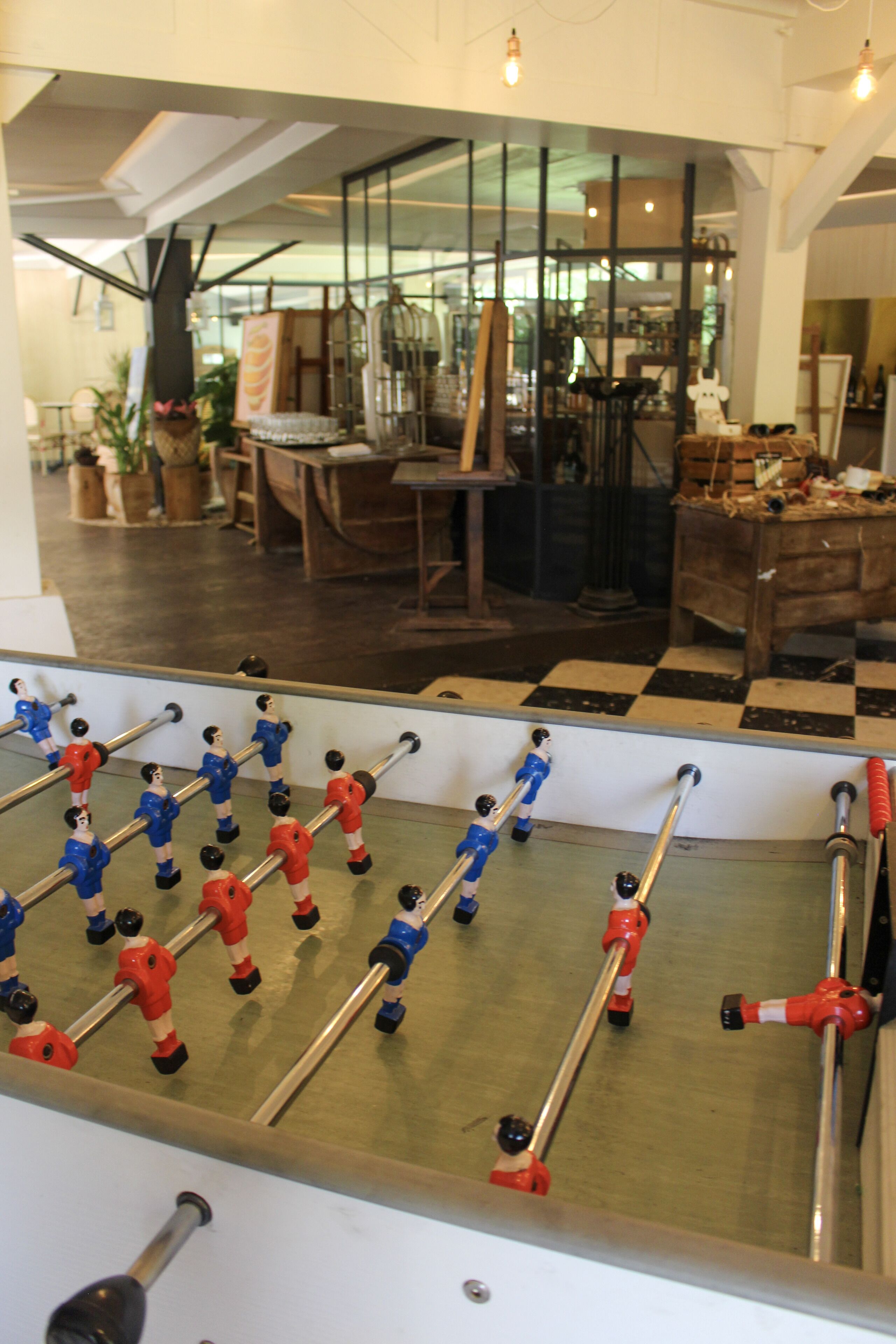 A foosball table in a room with a checkered floor, wooden furniture, and large windows.