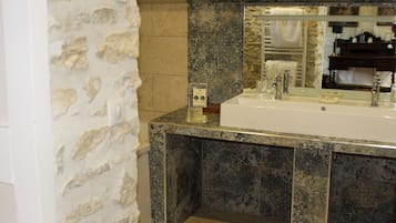 Une salle de bain avec un mur en pierre, un lavabo et un miroir.