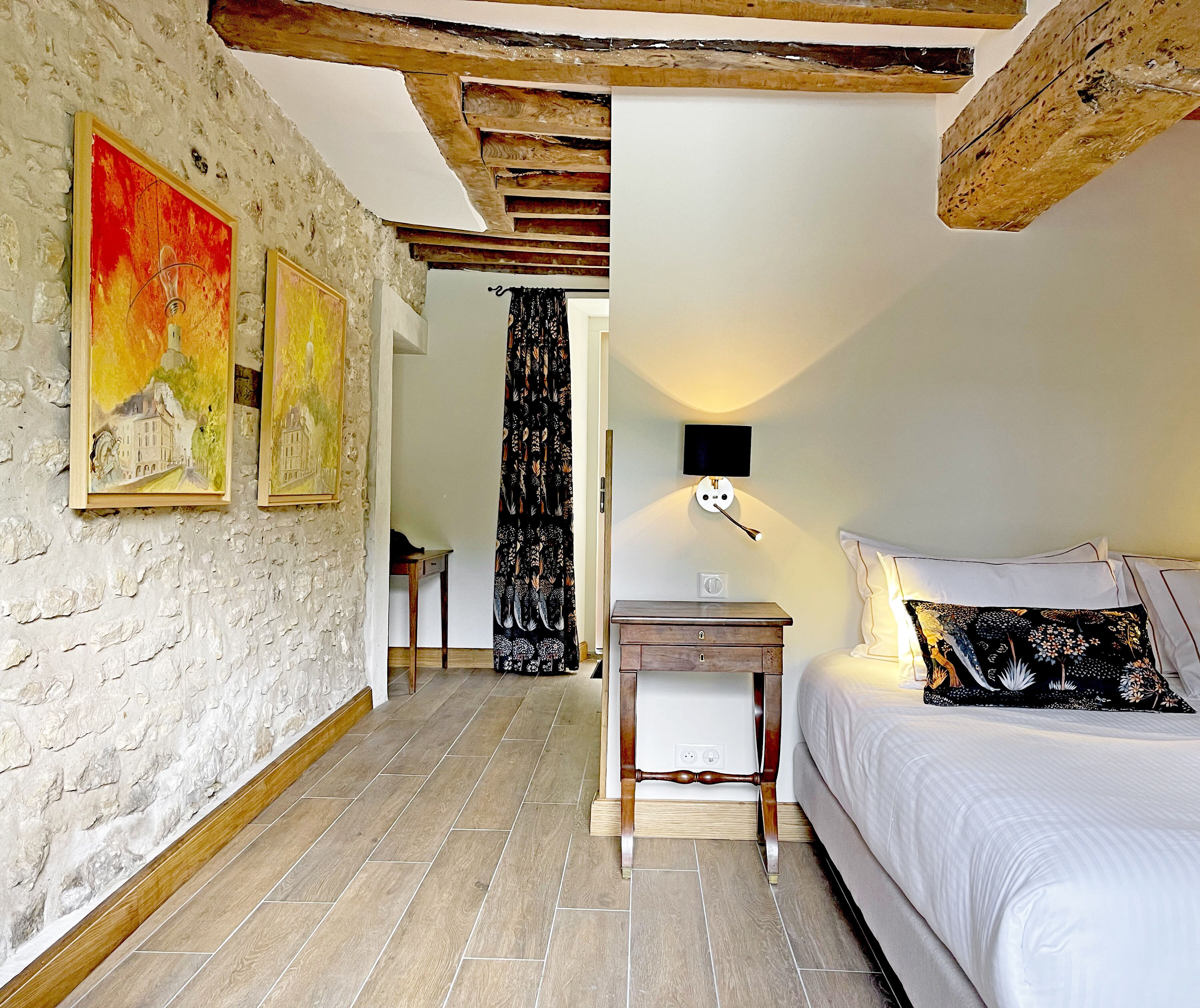 A bedroom with a bed, a nightstand, a wall-mounted lamp, and a painting on the wall.