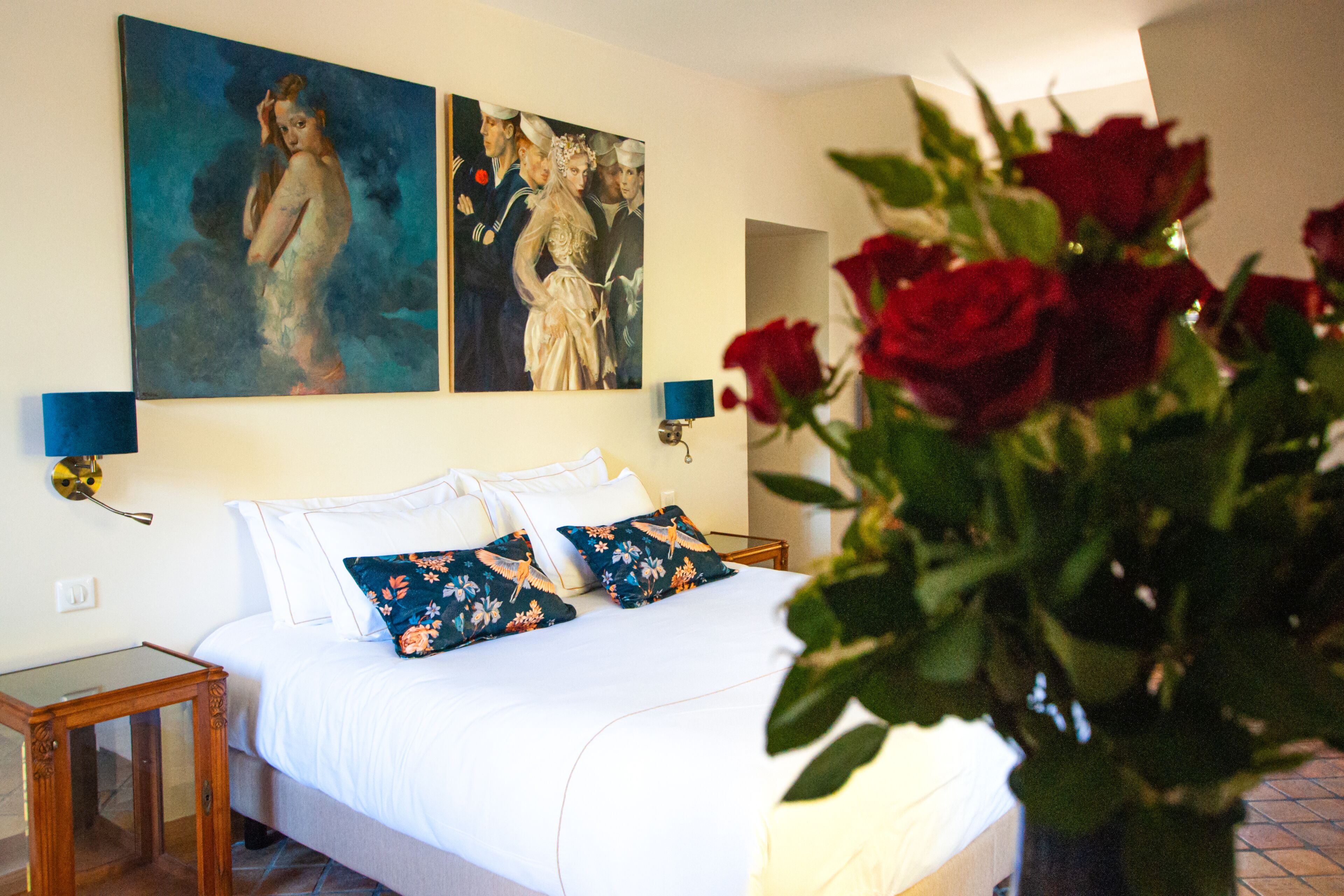 Een slaapkamer met een groot bed, twee wandlampen en een schilderij boven het bed.