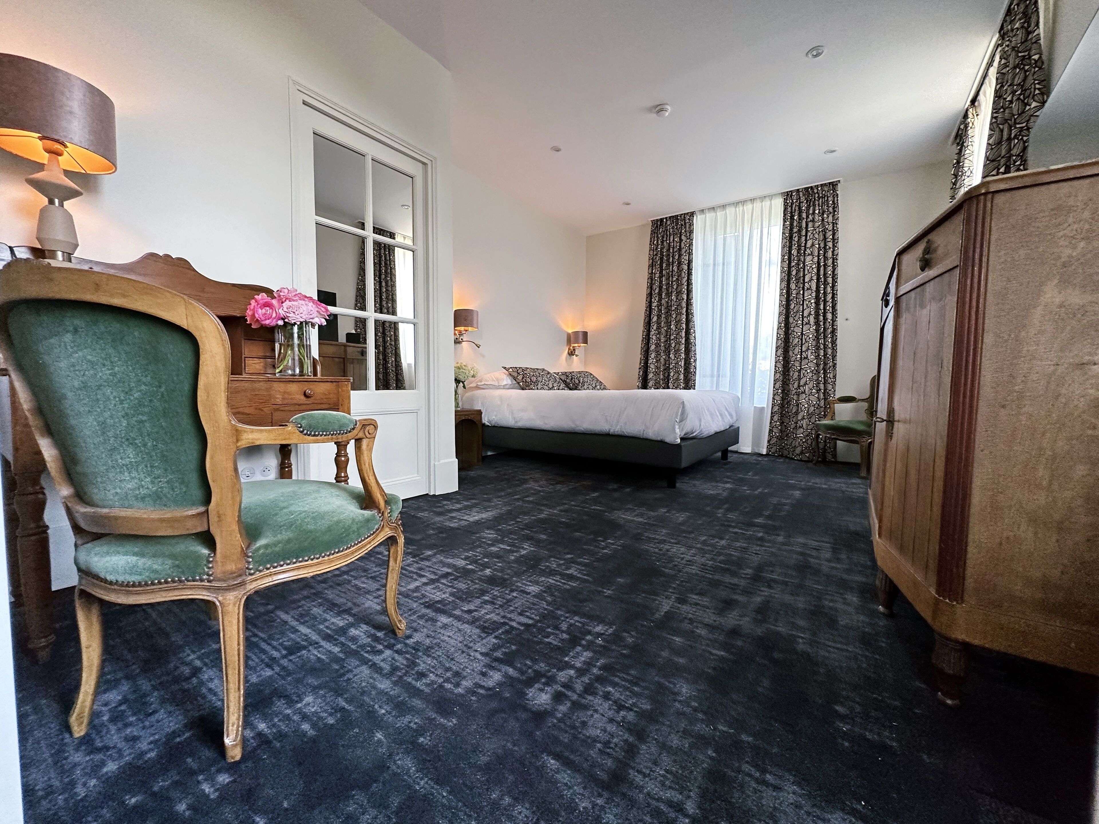 Una habitación de hotel con cama, una silla, un escritorio, una lámpara y un armario.
