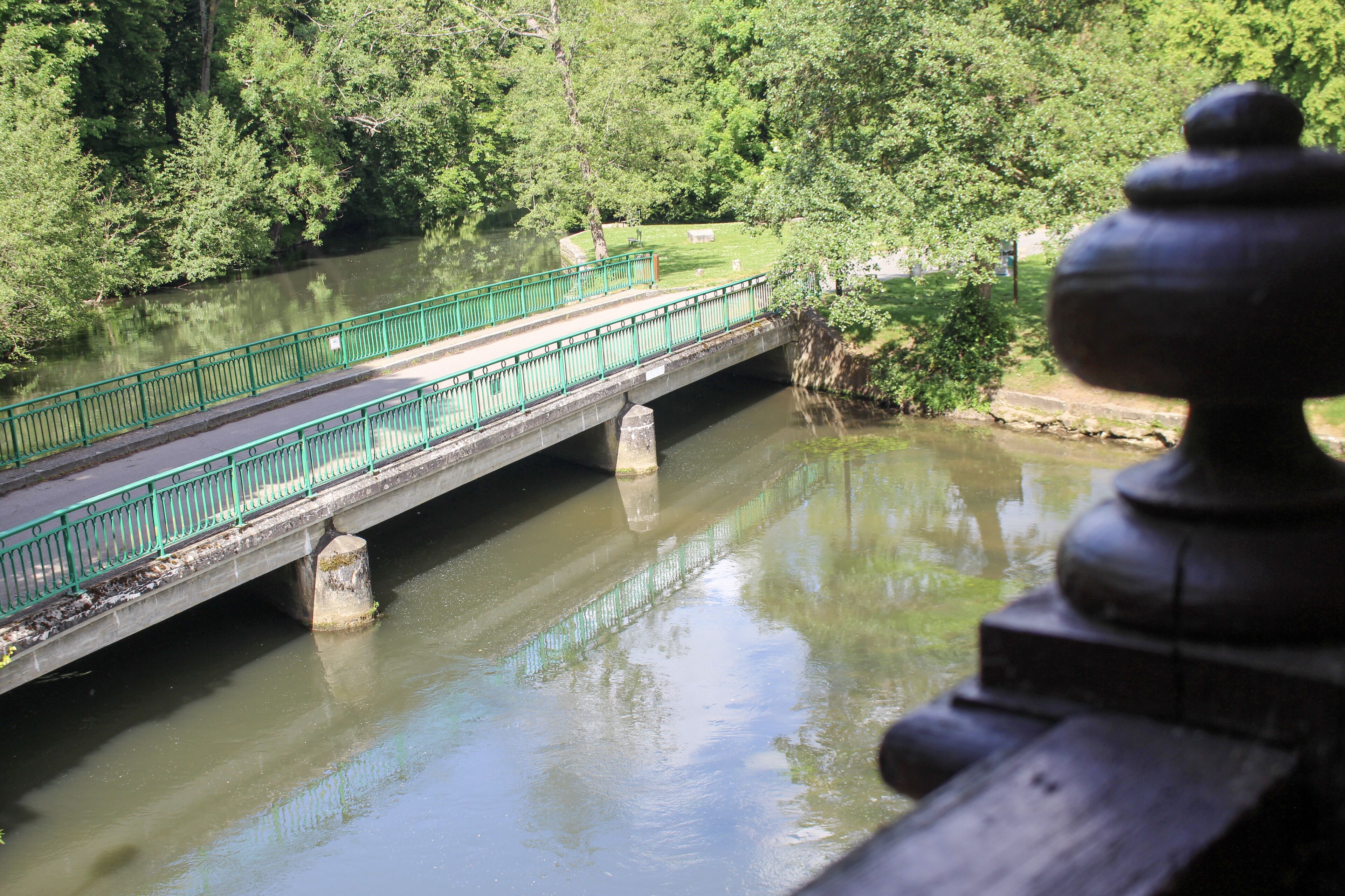 A bridge over a river with a green railing, surrounded by trees.