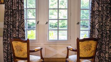 A room with two wooden chairs with floral upholstery, a white door with glass panels, and curtains with a floral pattern.