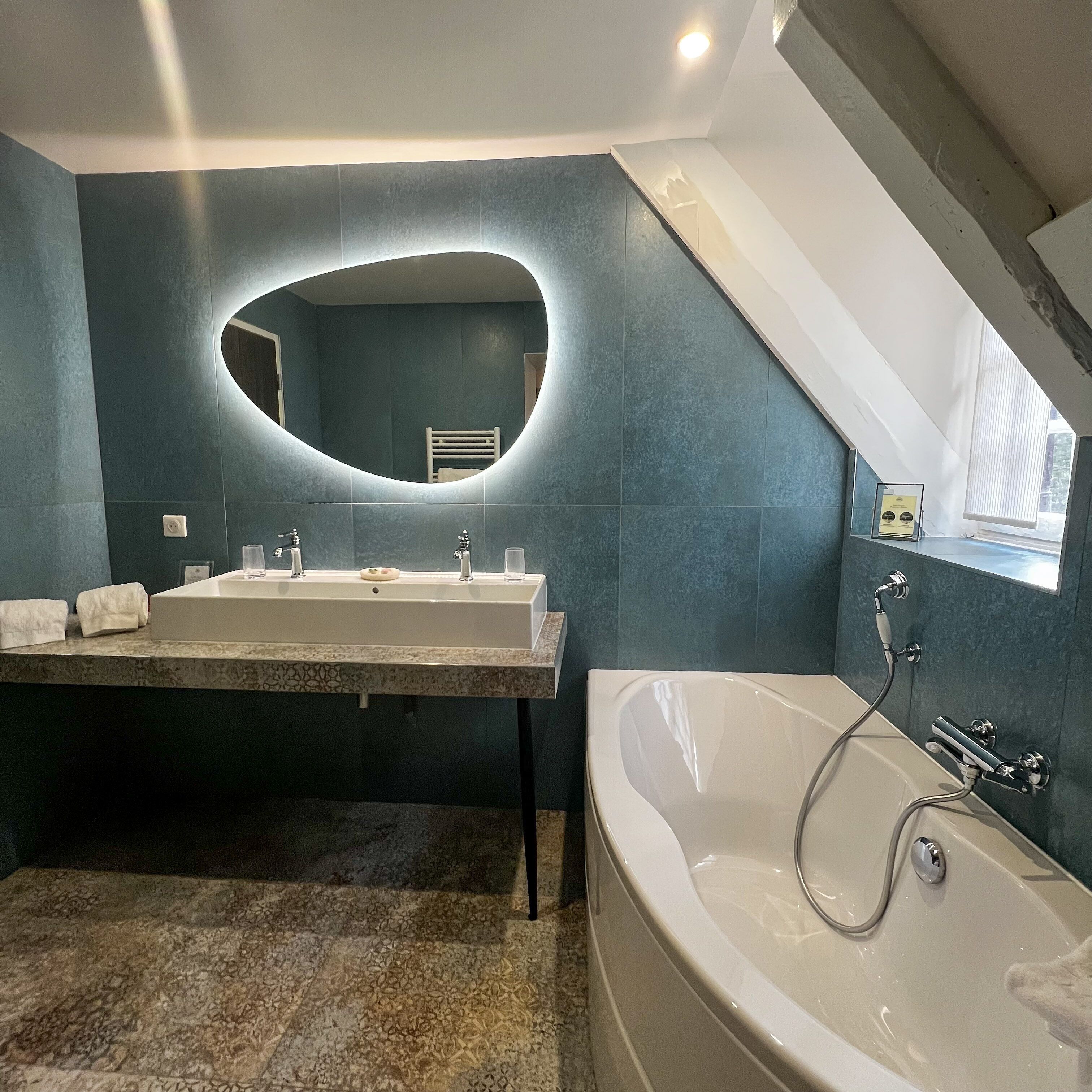 Un baño moderno con un espejo ovalado grande, lavamanos doble y una bañera independiente.