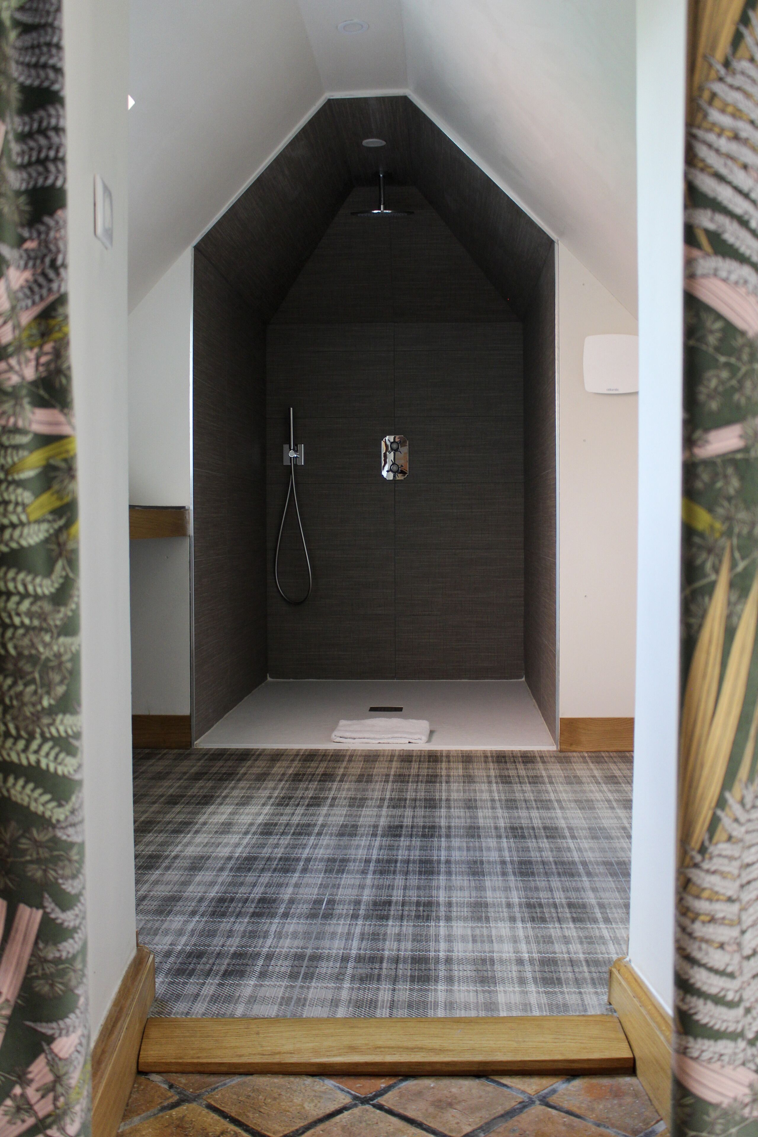 A small, sloped-roofed shower room with a checkered floor and a towel on the floor.