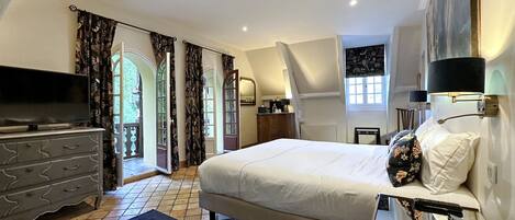 A bedroom with a bed, dresser, TV, and a view of the outdoors.