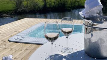 A wooden deck with a hot tub and two glasses of white wine, a bottle of champagne, and a pair of slippers.