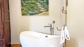Een badkamer met een vrijstaand bad, een houten kastje en een schilderij aan de muur.