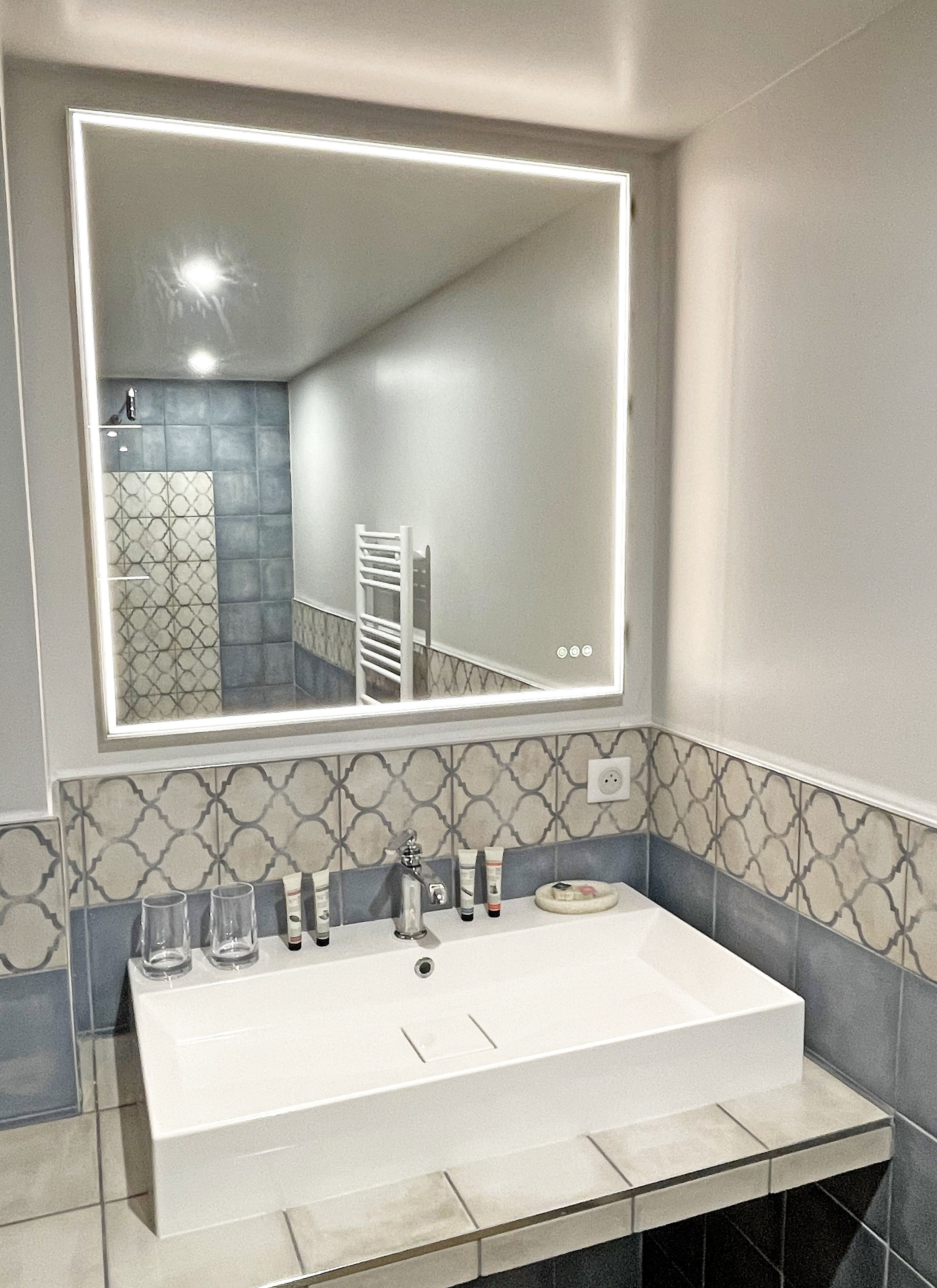 Un baño con un espejo grande, un lavabo blanco y azulejos estampados.