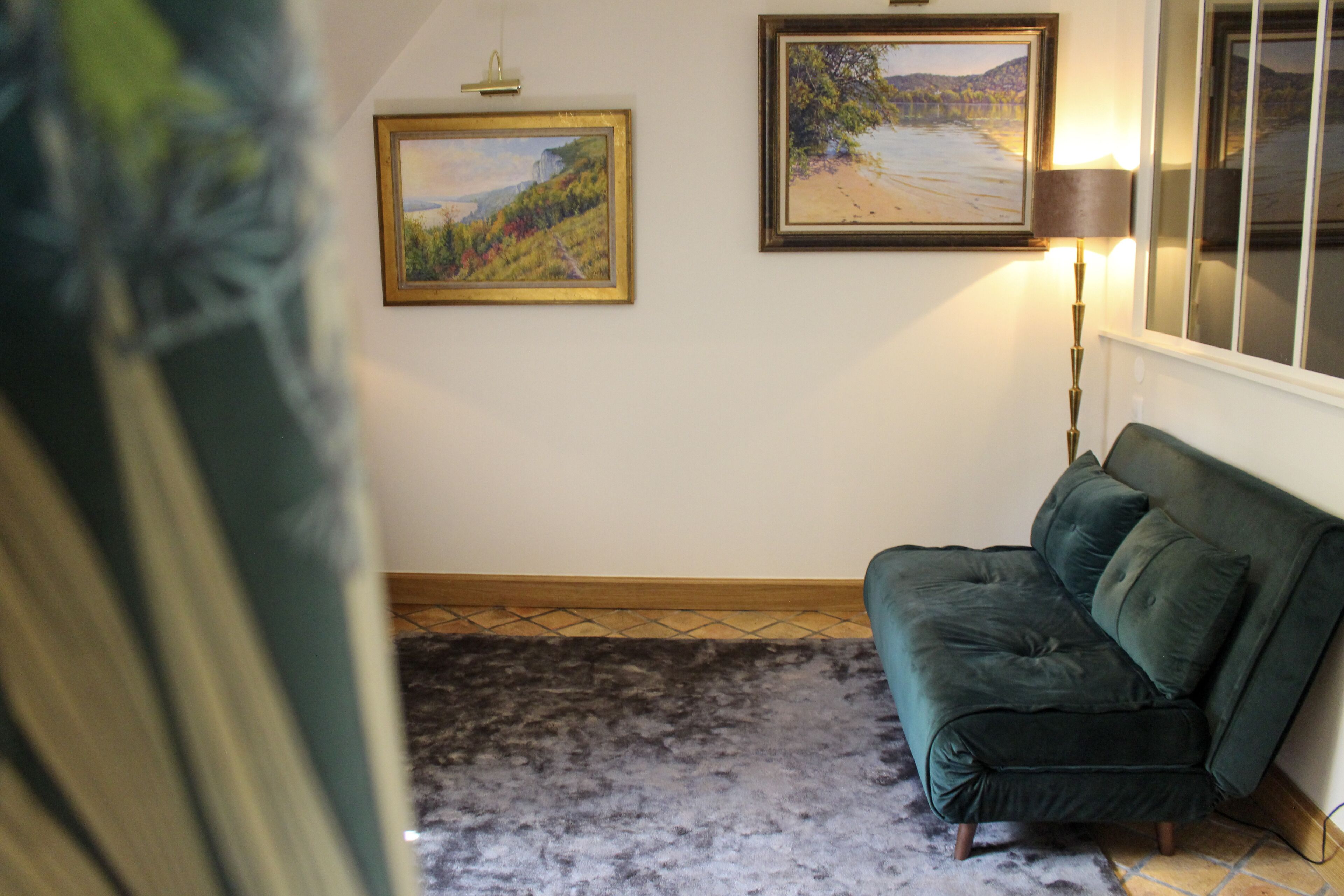 Ein Zimmer mit einem grünen Sofa, einem Teppich und zwei gerahmten Bildern an der Wand.