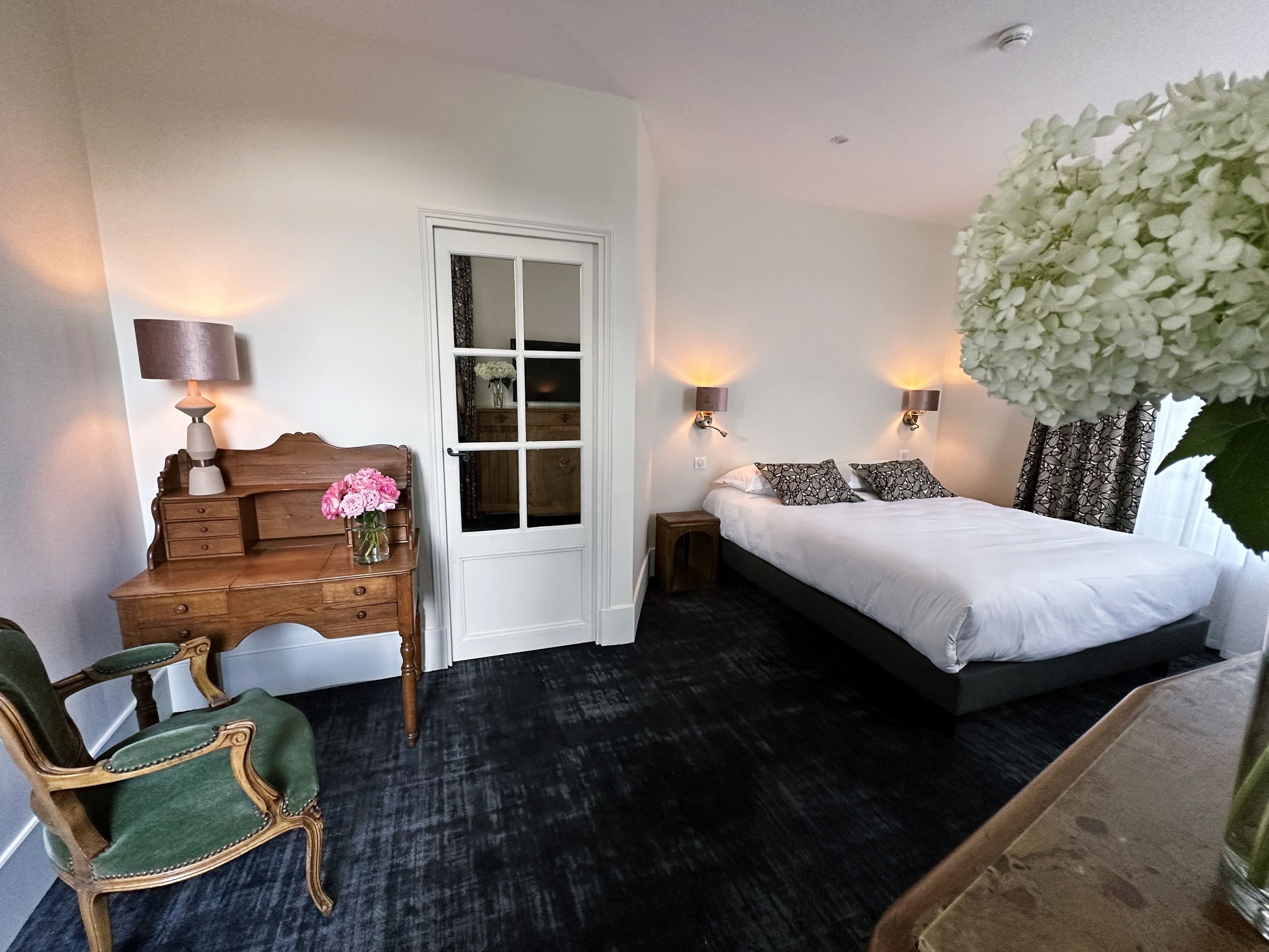 A bedroom with a bed, a wooden dresser, a chair, a nightstand, and a door.