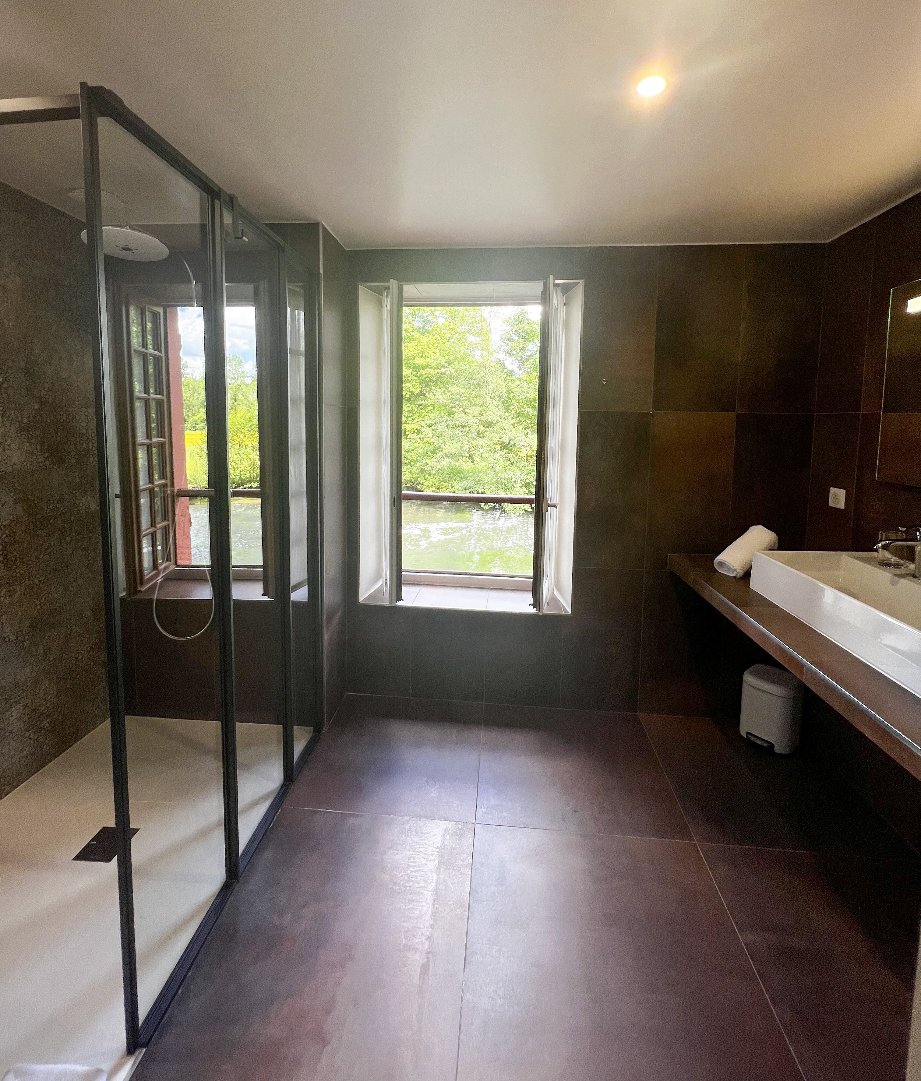 A modern bathroom with a glass shower enclosure, a large window, and a vanity with a mirror.