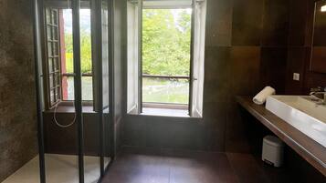 A modern bathroom with a glass shower enclosure, a large window, and a vanity with a mirror.