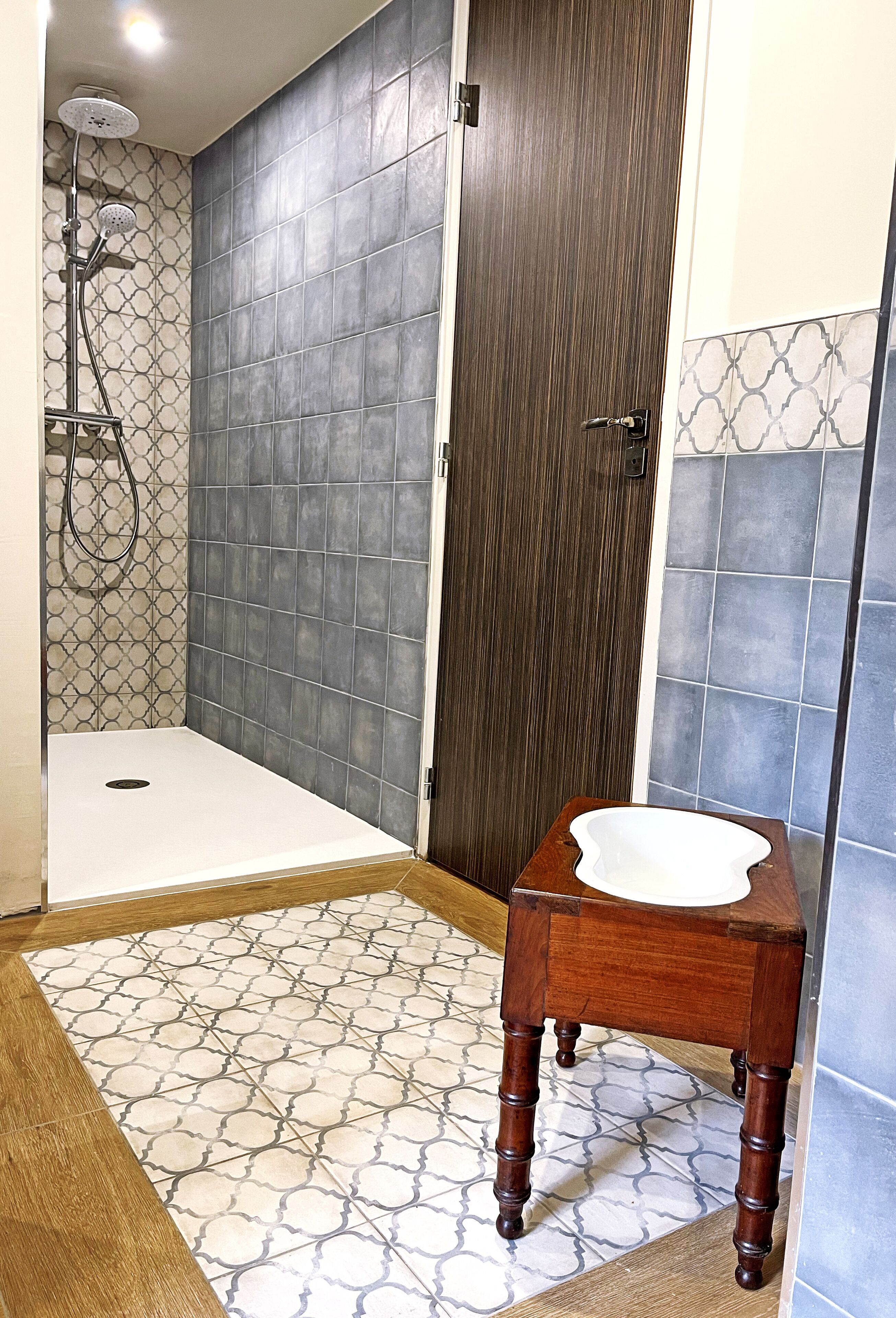 A bathroom with a shower, a wooden vanity, and patterned tiles.
