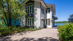 A two-story house with a paved driveway, large windows, and a view of a lake. - 3 Bedroom | Beachwalk Resort House on Lake Kai (Michigan City)