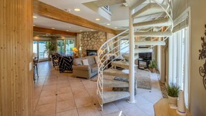 A spacious living area with a spiral staircase, a stone wall, and a cozy seating area with a sofa and armchairs. - 3 Bedroom | Beachwalk Resort House on Lake Kai (Michigan City)