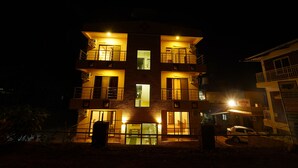 A multi-story building with illuminated windows and balconies, a visible staircase, and a parked car in front. - Treebo Infinity View Mahabaleswar (Jaoli)