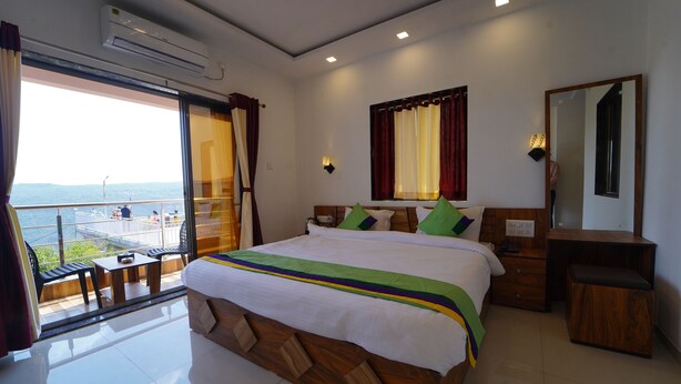 A modern hotel room with a large bed, a desk, a chair, and a balcony with a view of the sea. - Treebo Infinity View Mahabaleswar (Jaoli)
