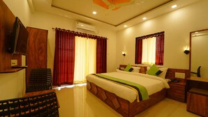 A hotel room with a large bed, wooden headboard, red curtains, a flat-screen TV, a bedside table, and a mirror. - Treebo Infinity View Mahabaleswar (Jaoli)