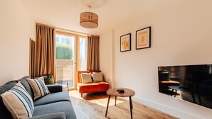A modern living room with a grey sofa, an orange armchair, a small round table, and a large flat-screen TV mounted on the wall. - Redland Stay In Bespoke Home 2 of 2 (Bristol)