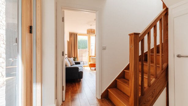 A hallway with wooden flooring, a staircase with wooden railings, and a sofa in the background. - Redland Stay In Bespoke Home 2 of 2 (Bristol)