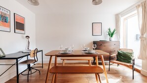 A modern dining area with a wooden table set for two, a black chair, a wicker chair, and a bench. There are two pendant lights, a potted plant, and a framed picture on the wall. - Redland Stay In Bespoke Home 2 of 2 (Bristol)