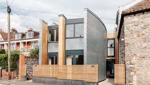 A modern two-story house with a curved glass facade, wooden slatted fence, and stone walls. - Redland Stay In Bespoke Home 2 of 2 (Bristol)