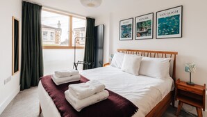 A hotel room with a large bed, a window with curtains, a bedside table, and artwork on the wall. - Redland Stay In Bespoke Home 2 of 2 (Bristol)