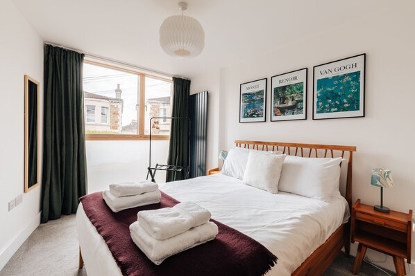 A hotel room with a large bed, a window with curtains, a bedside table, and artwork on the wall.