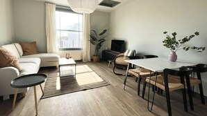 Ett modernt vardagsrum med en soffa, ett soffbord, ett matbord, stolar, en tv och ett stort fönster med gardiner.