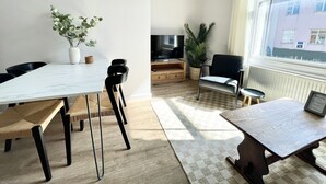 A modern living room with a dining area, a TV, and a large window with a city view. - Spacious and Stylish Central Bristol Base (Bristol)