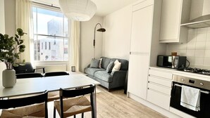 A modern kitchen with white cabinets, a dining table with chairs, a sofa, and a view of buildings outside. - Spacious and Stylish Central Bristol Base (Bristol)