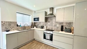 A modern kitchen with white cabinets, a built-in oven, a microwave, and a tiled backsplash. - Beautiful Cosy Rural Retreat with Parking! (Winford)