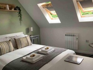 A bedroom with a bed, two skylights, a radiator, and a bedside table with a lamp.