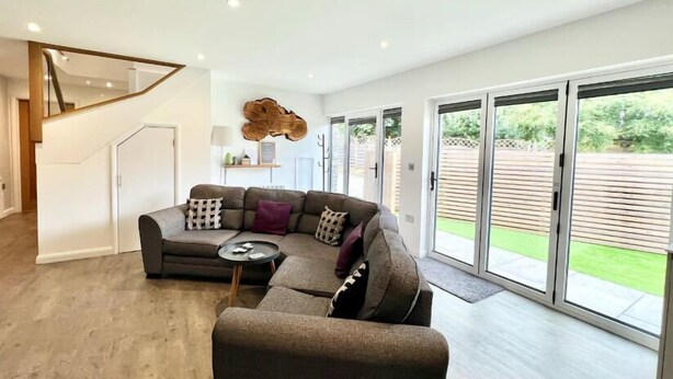 A modern living room with a sectional sofa, a small side table, and a large sliding glass door leading to a backyard. - Beautiful Cosy Rural Retreat with Parking! (Winford)