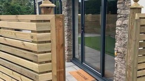 A modern building with a stone facade, a wooden gate, and a welcome mat. - Beautiful Cosy Rural Retreat with Parking! (Winford)