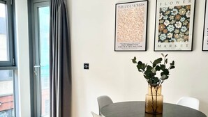 A dining area with a round table, four chairs, and a vase with greenery. There are two framed artworks on the wall. - Modern apartment in Bristol City Centre (Bristol)