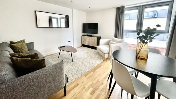 A modern living room with a grey sofa, a small round table, a white armchair, and a TV on a cabinet. - Modern apartment in Bristol City Centre (Bristol)