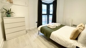 A modern bedroom with a bed, a dresser, a potted plant, a window with curtains, and a radiator. - Modern apartment in Bristol City Centre (Bristol)