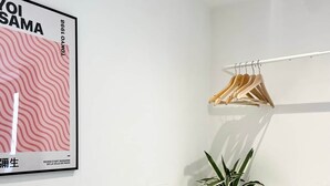 A minimalist room with a white wall, a poster, wooden hangers, and a potted plant. - Modern apartment in Bristol City Centre (Bristol)