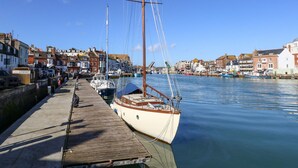 A harbor with boats docked along a wooden pier, surrounded by buildings with a mix of architectural styles. - Park Mews (Weymouth)
