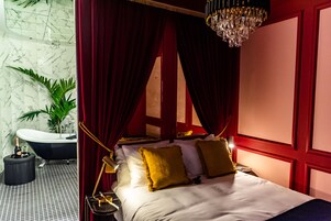 Un dormitorio lujoso con cama con dosel, cortinas rojas y un candelabro.