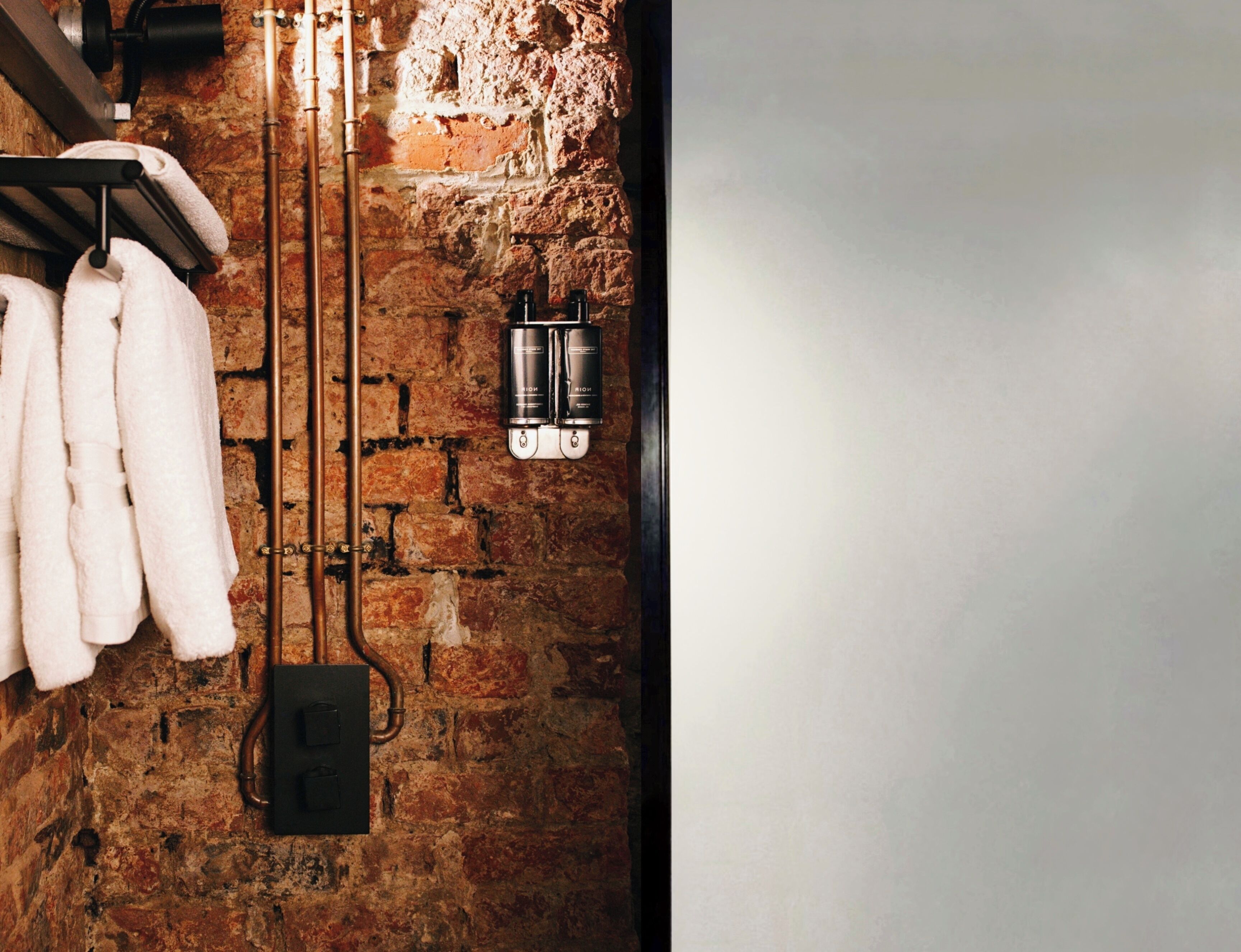 A bathroom with a brick wall, a towel rack with white towels, a black faucet, and a water dispenser.