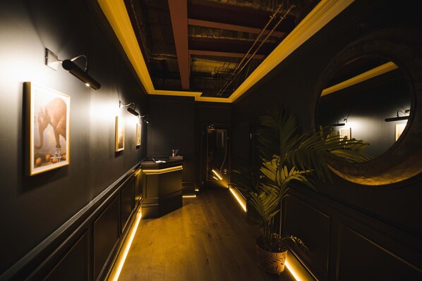 A hallway with a reception desk, framed artwork on the walls, a large mirror, and a potted plant. - Impossible Motel (York)
