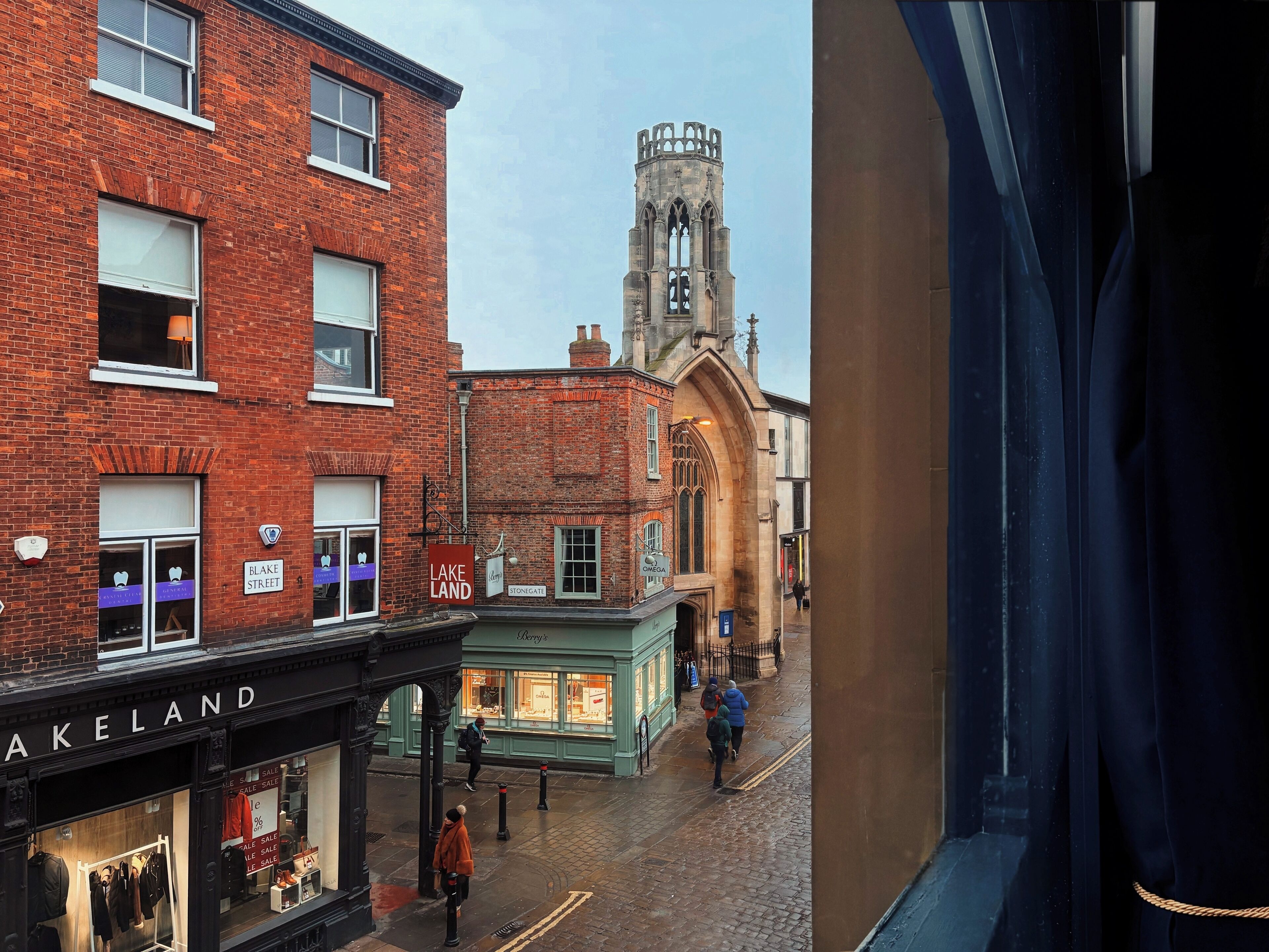 A street view with a mix of modern and historic buildings, including a prominent tower with a clock.
