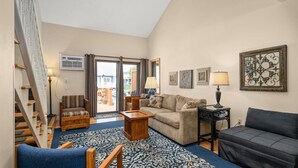 A spacious living room with a sofa, armchair, and coffee table, a staircase, and a view through glass doors to the outside. - 1 BR 1.5 Canal Front Unit with Pool! (Ocean City)
